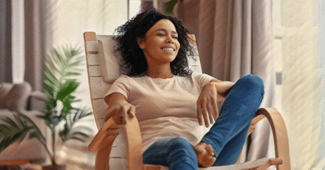 A woman relaxes in a chair in the middle of her living room, smile on her face