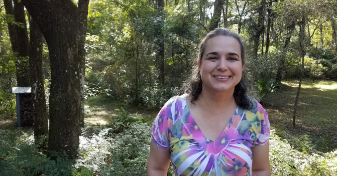 A woman stands in front of a yard with a lot of trees.