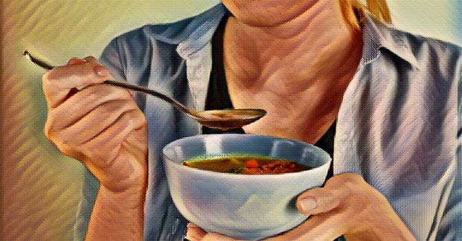 woman cups a bowl of soup in her left hand and lifts a spoonful of soup with her right her mouth