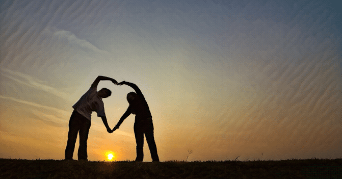 a couple form a heart with their arms as the sun sets in the background.