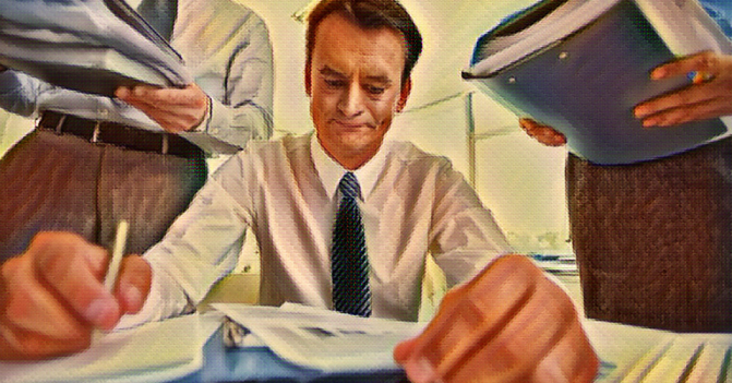 man at desk working with two people standing beside him about to dump huge binders of more work on his desk