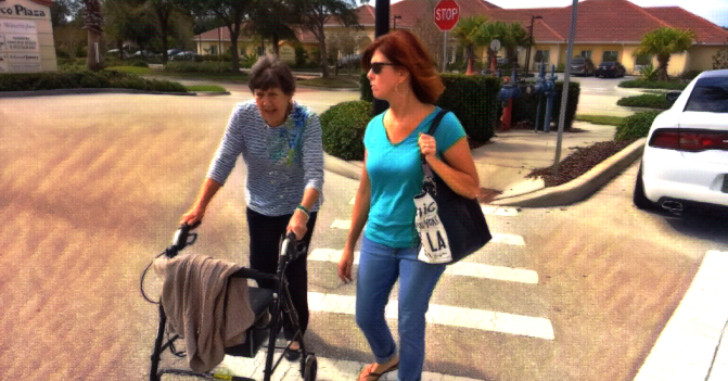 My mother, in her older age, uses a walker to cross the street alongside my sister Trish.