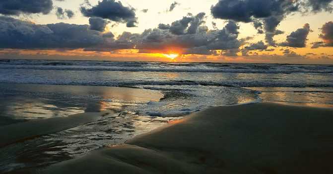 a runnel or rivulet on the beach forces waves to flow water into it to feed a tide pool. The sun is rising in a sky scattered with fluffy clouds