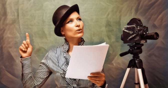 Woman wearing a top hat stands before a camera with a script in hand