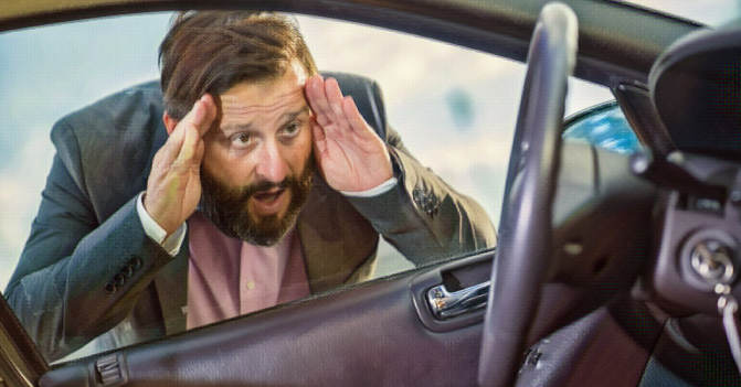 a man presses against his locked car's drivers side window looking dismayed to see the keys in the ignition
