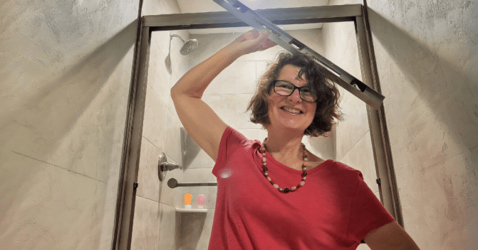 The author stands in front of her new shower, holding a level in her right hand above her head -- and not level. She is smiling.