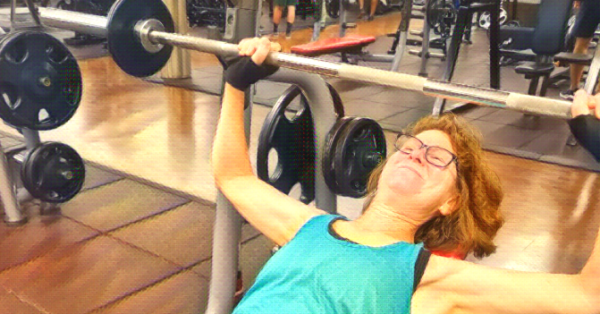 Woman grimaces as she tries to lift weight on the incline chest press machine