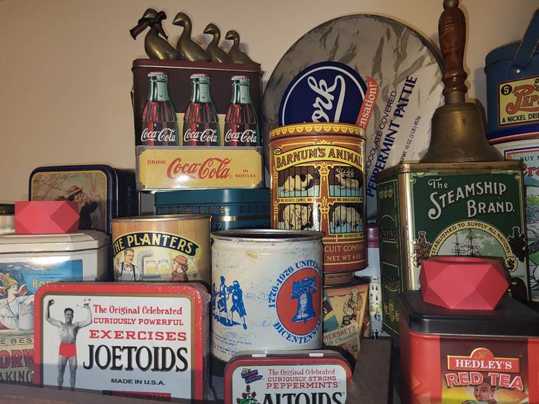 The image shows a display of product tins decades old, with a tin from 1976 depicting the bicentennial, showing the Liberty Bell and the Sons of Liberty.